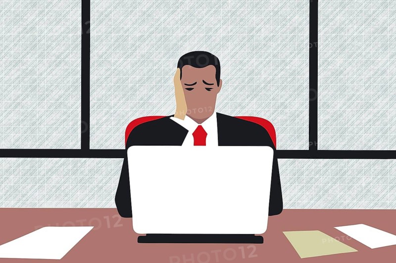 A business professional at a desk shows signs of stress and depression while working on a laptop. The modern office environment features large windows and a simple layout