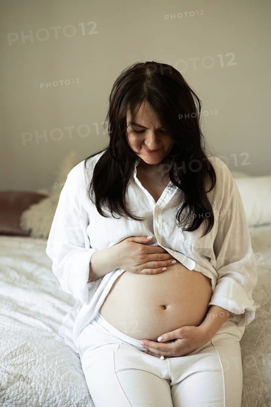 A serene pregnant woman in a relaxed setting, embracing her growing belly. She is preparing for the journey of motherhood, radiating joy and anticipation for the new life