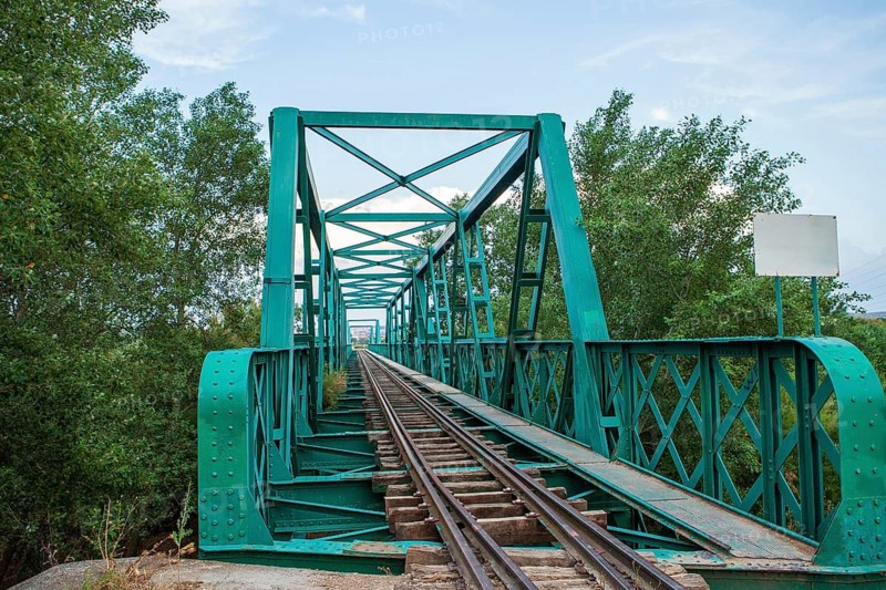 An aged green railroad bridge with rust and weathering stretches over lush foliage, exemplifying a blend of history and nature