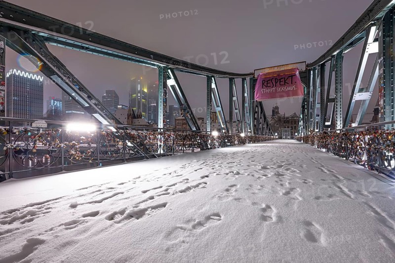 Snow lies on the Iron Bridge in Frankfurt am Main. The skyscrapers of Frankfurt's banking skyline can be seen through the steel framework of the bridge. Frankfurt am Main, Hesse, Germany