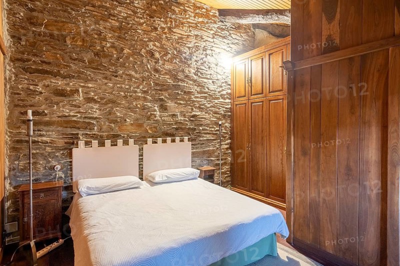 Charming bedroom featuring rustic stone walls and wooden furniture, located in a country house in Lugo, Spain. The room's unique architecture highlights its historical charm