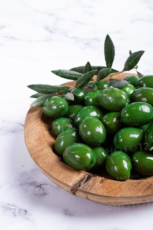Halkidiki olives, classic Greek green olives, in a wooden bowl, on a marble table, no people