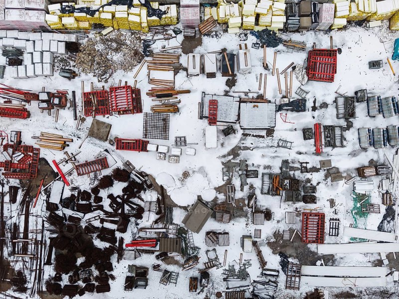 High angle aerial view of a construction site or industrial storage yard with various materials and equipment scattered on snow-covered ground in Lubin, Poland