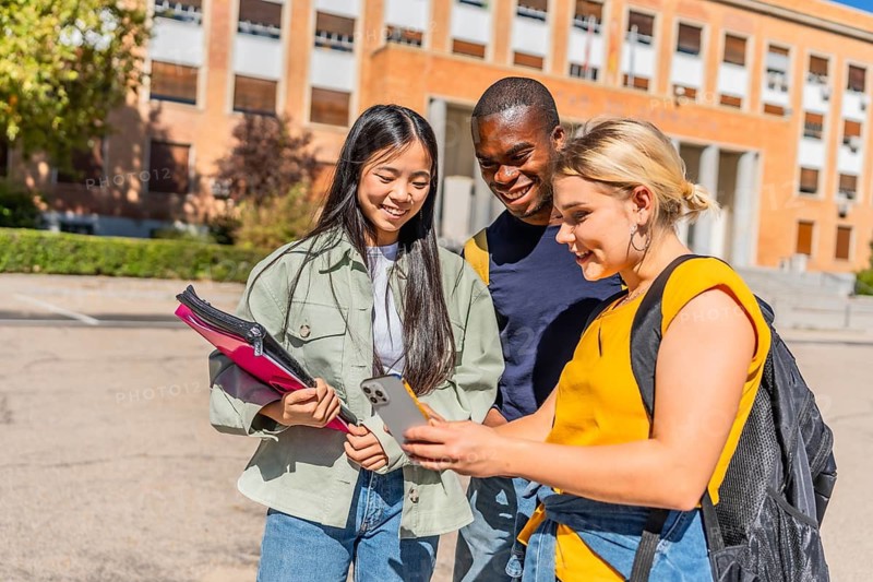 Three multi-ethnic students looking at the mobile phone together standing in the campus