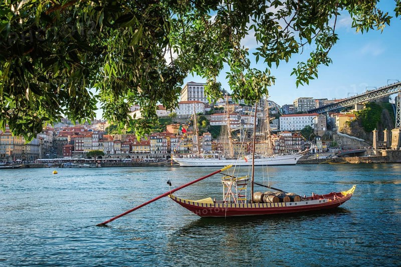 View of Porto city and Douro river with traditional boats with port wine barrels and sailing ship from famous tourist viewpoint Marginal de Gaia riverfront. Porto, Vila Nova de Gaia, Portugal