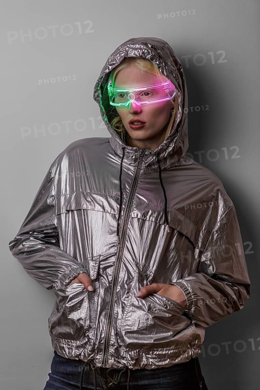 A woman wearing neon-lit glasses and a reflective jacket, embodying a futuristic and high-tech style. The vibrant colors and shiny fabric create a striking visual effect