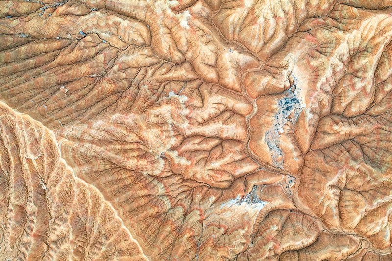 An aerial view showcases a rugged desert landscape marked by intricate erosion patterns The arid terrain features varying shades of brown and subtle geological textures