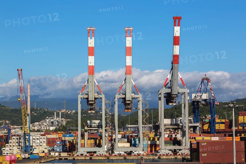 Tall red, white and grey gantry cranes and stacked rectangular metal box shipping containers on dock in La Spezia cargo Port, Italy