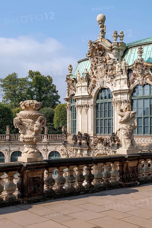 A detailed view of the ornate Baroque architecture of the Palace Zwinger in Dresden, Germany, showcasing its intricate statues and elaborate design set against a clear sky