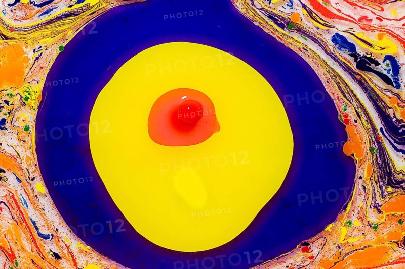 A vibrant paint swirls in bold blues and yellows, centered by a red dot, resembling a modern, abstract artwork with a dynamic color mixture