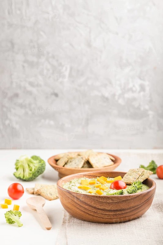 Green broccoli cream soup with crackers and cheese in wooden bowl on a white and gray background and linen napkin. side view, copy space
