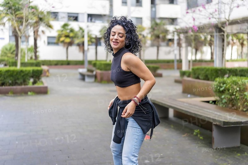 Curly haired dancer practicing modern dance moves in an urban park, enjoying freedom and self expression through movement