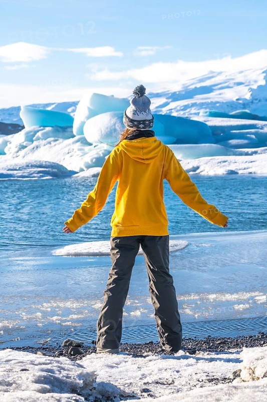 A woman with her back turned on the frozen lake Jokulsarlon during her vacation in Iceland, vertical photo