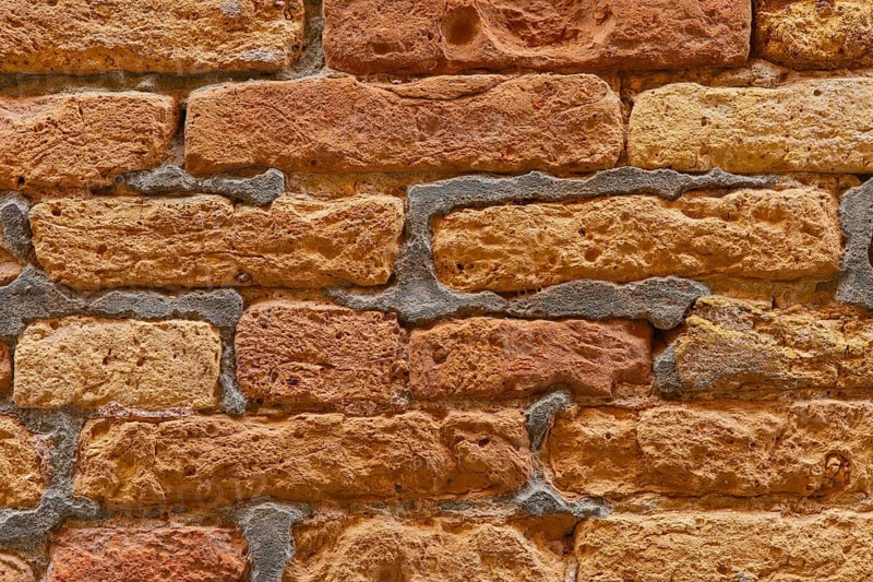 Close-up view of a rustic brick wall, showcasing its unique textured pattern with rough surfaces. The orange and brown hues enhance its natural appearance and tactile appeal