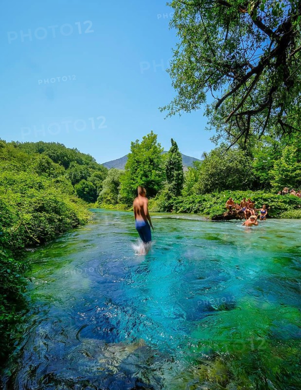Muzina, Albania, tourists bathe in the Syri i Kaltër, THE BLUE EYE, is the country's most water-rich spring at 6 metres per second. The water emerges from a spring pot at a depth of more than 50 metres under high pressure. The water temperature is a fairly constant 12.75°C. The Blue Eye is located midway between the larger towns of Saranda on the coast and Gjirokastra inland