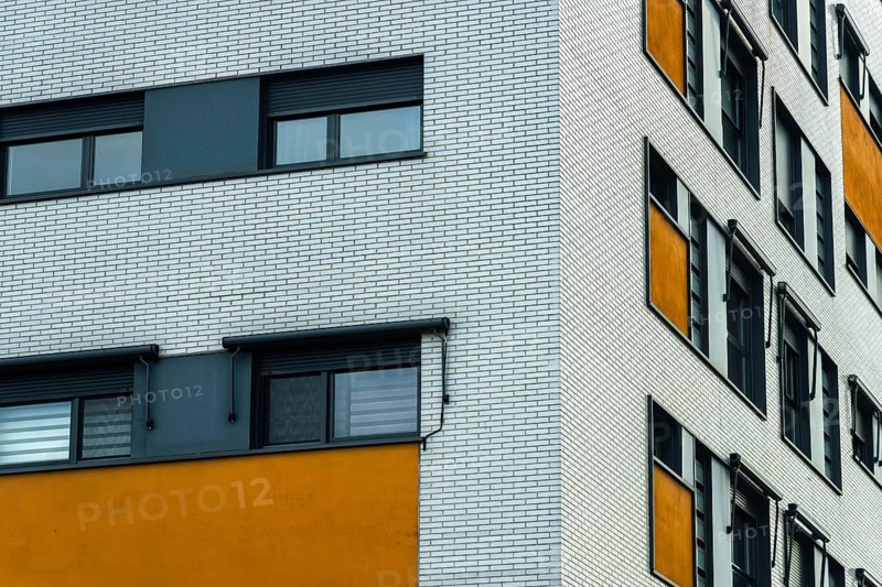 A modern building facade with a distinct design, a white brick wall with sleek, dark windows and a sandy orange section, bringing a pop of color to the cityscape