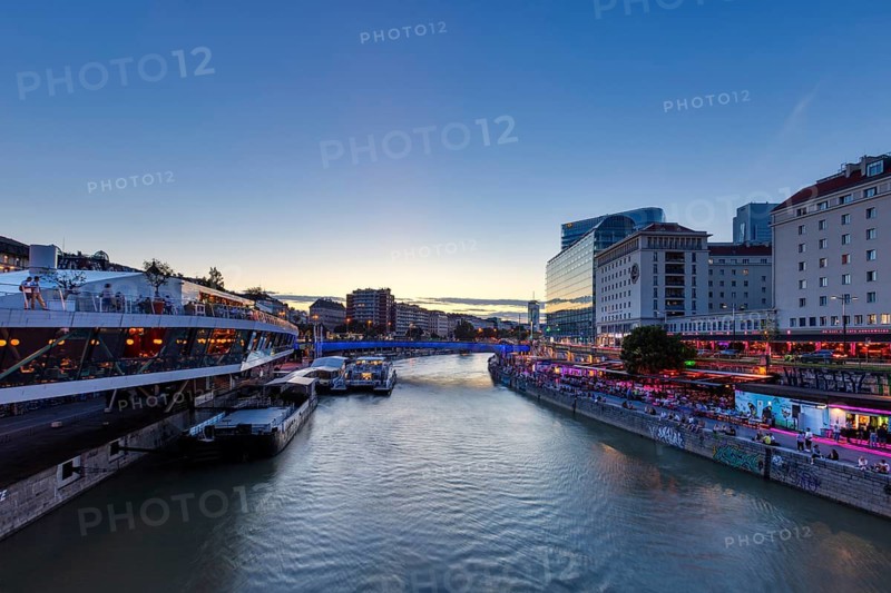 City view at dusk with illuminated buildings along a quiet river, Vienna
