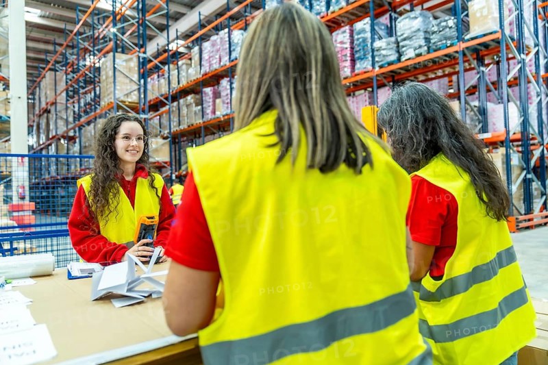 Three females factory workers pack packages for delivery in a distribution warehouse