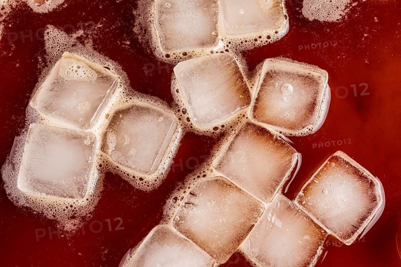 Top view of transparent ice cubes floating in rich, dark cold brew coffee. The iced beverage creates a refreshing and invigorating backdrop, perfect for showcasing chilled drinks
