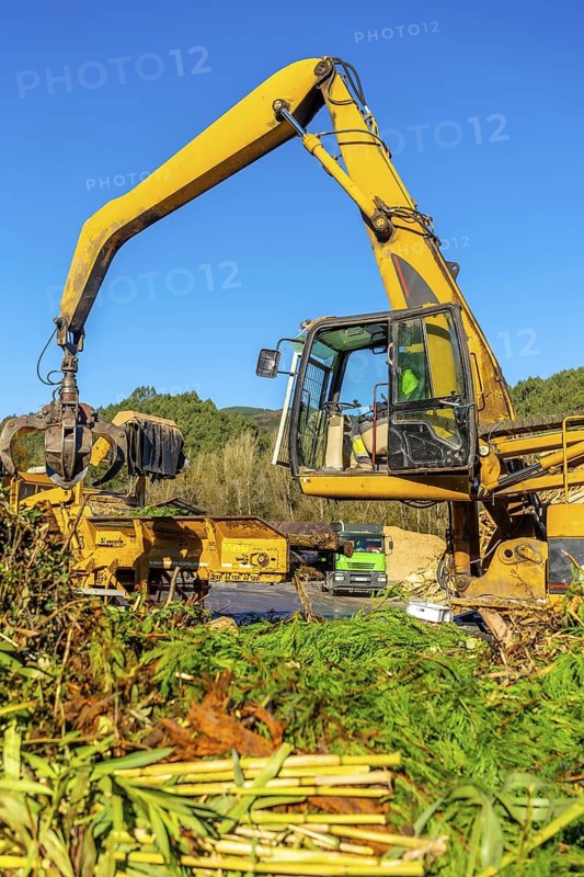 Vertical full length photo of a manual male worker driving an excavator working outside a recycling plant in a sunny day