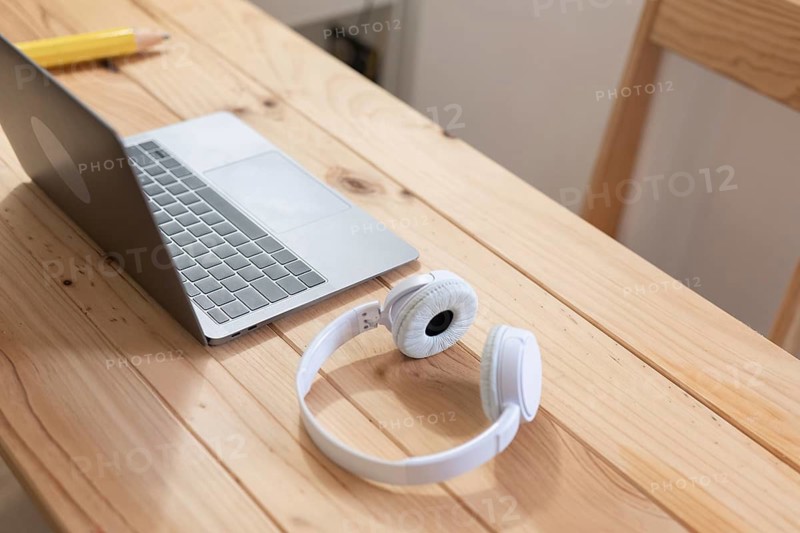 A minimalist workspace with a sleek laptop and white headphones on a light wooden desk. Ideal for representing modern work, technology, and productivity themes