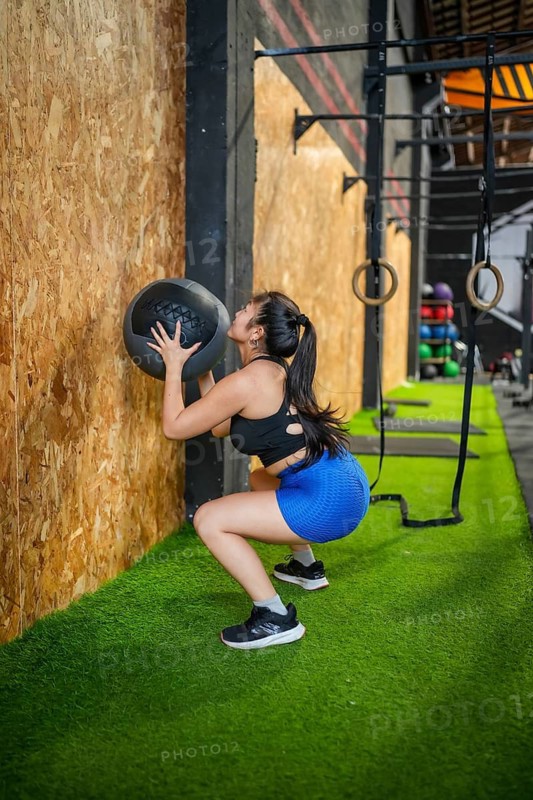 Full length side view of an asian sportive woman working out in a gym using medicine ball