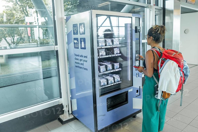 A traveler with a backpack uses a vending machine at an airport to purchase masks and sanitizers The well-lit terminal highlights modern travel essentials and safety