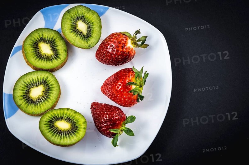 Sliced kiwis and strawberries on a white plate with a black background