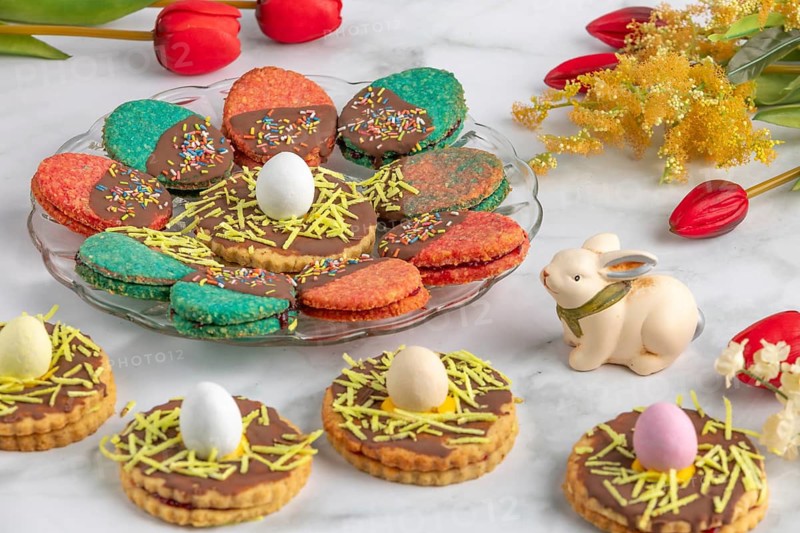 Plate with colourful Easter biscuits, decorated with eggs, next to red tulips