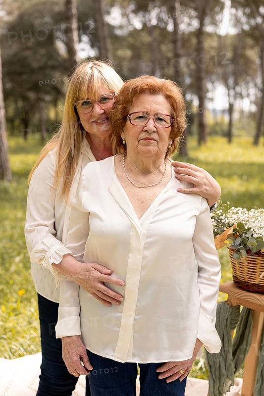 A daughter affectionately embraces her elderly mother in a peaceful outdoor environment, surrounded by lush greenery, symbolizing love and family bond