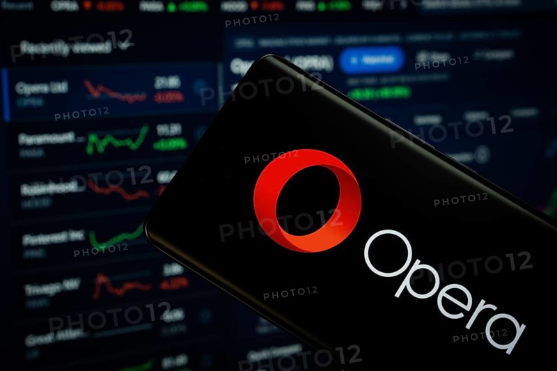 Dhaka, Bangladesh- 17 March 2025: opera logo is displayed on a smartphone screen, with a stock graph webpage visible on a computer screen in the background
