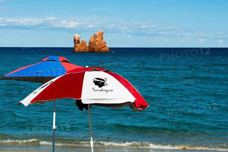 Sunshades on the beach and red rocks, Spiaggia di Cea, Tortoli, Sardinia, Italy