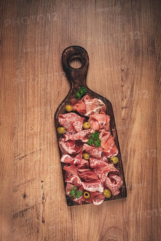 Assortment, sliced meat appetizer, prosciutto, salami and ham, with olives, on a wooden board, breakfast, top view, close-up, no people