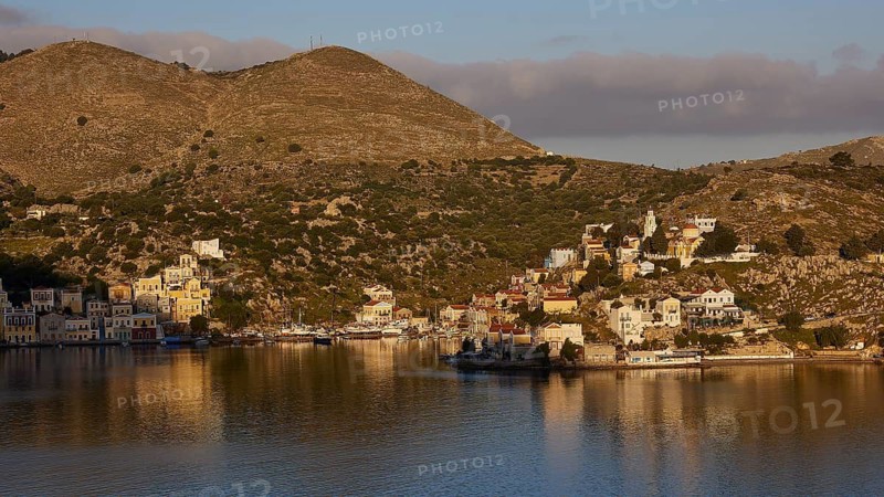 Small village by the water and foot of the hill, bathed in warm sunlight, Symi Town, Symi, Dodecanese, Greek Islands, Greece