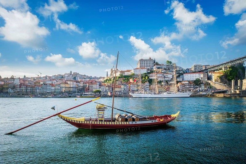 View of Porto city and Douro river with traditional boats with port wine barrels and sailing ship from famous tourist viewpoint Marginal de Gaia riverfront. Porto, Vila Nova de Gaia, Portugal