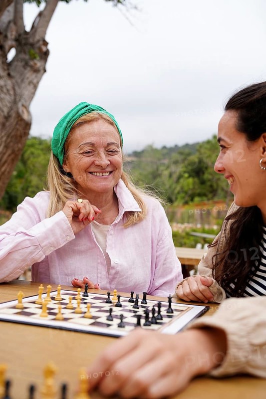 Mother and daughter enjoy a friendly game of chess in a peaceful outdoor setting Laughter and strategy fill the air as they focus on the board, surrounded by lush greenery