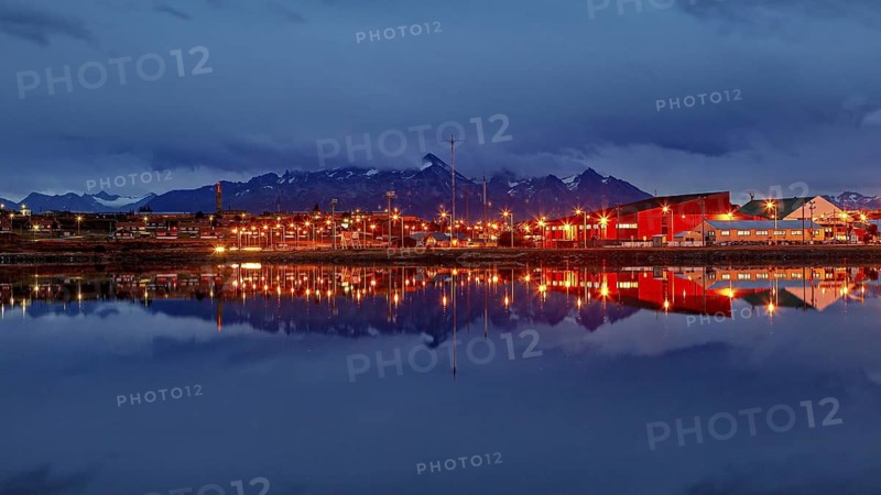 Night view of a city with glowing lights and mountain silhouette reflected in the water, The city of Ushuaia in Argentina is reflected in the sea