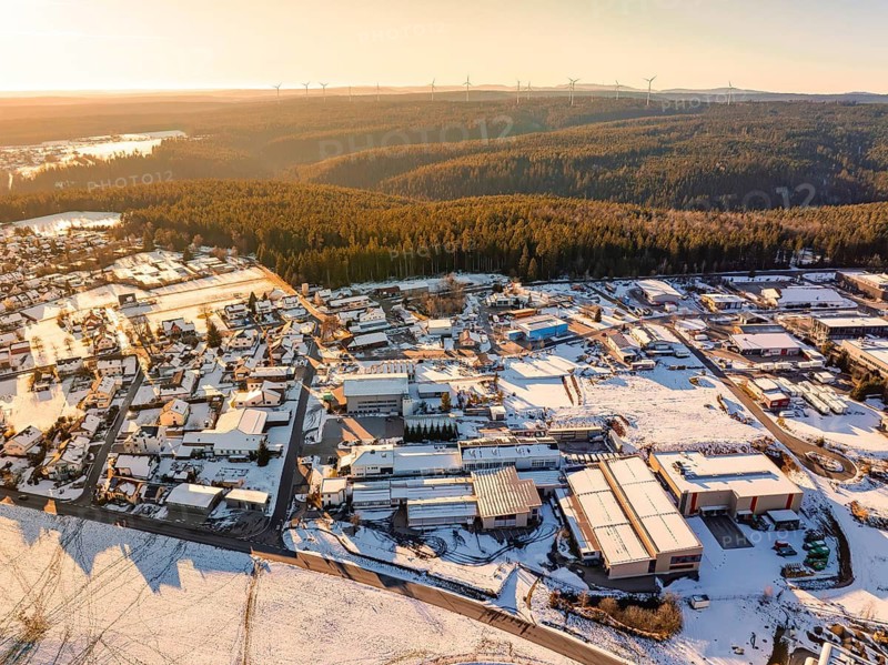 Industrial area next to a forest, with snow-covered roofs and fields under warm evening light, Simmersfeld, district of Calw, Black Forest, Germany