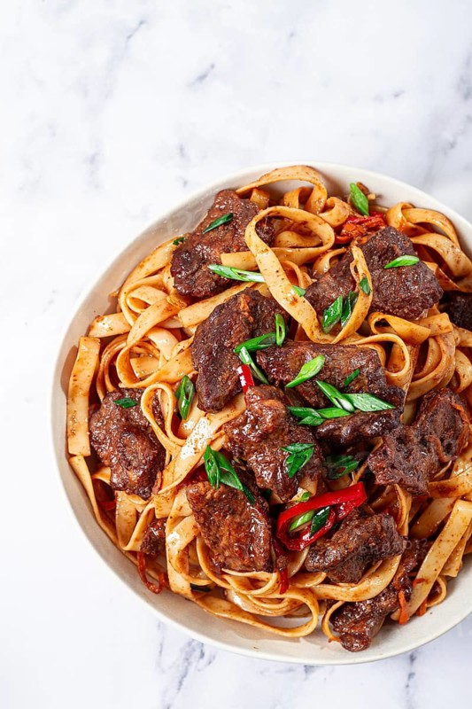 Udon noodles with Mongolian beef, green onions and vegetables, in a white plate, on a light background, homemade, no people