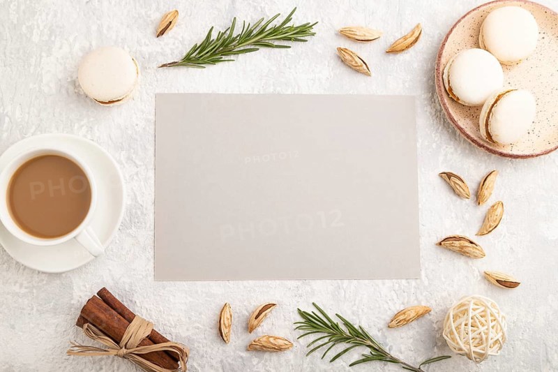 Gray paper sheet mockup with cup of coffee, almonds and macaroons on gray concrete background. Blank, business card, top view, flat lay, still life