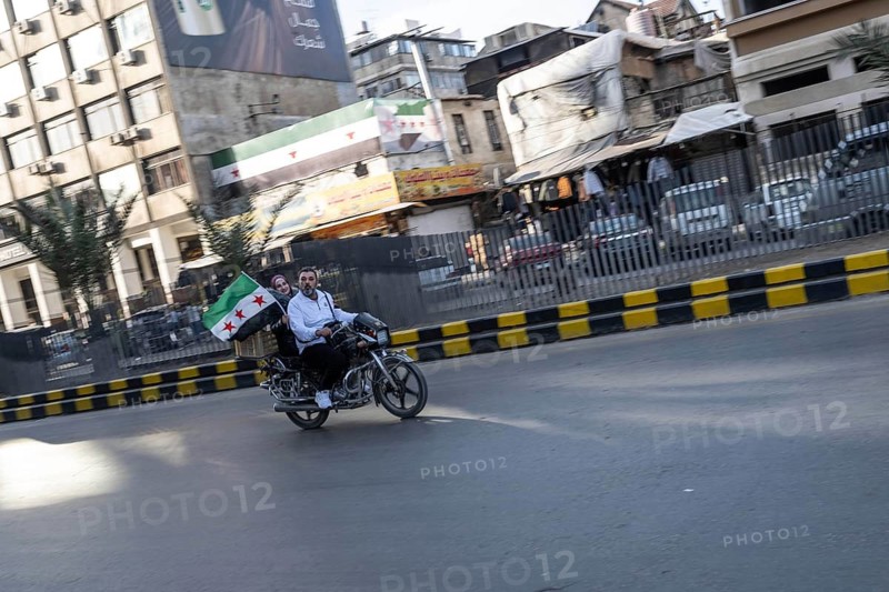 Damascus, Syria. December 5th 2025. A Syrian man and woman ride a motorcycle with a Syrian flag through the streets of Damascus in celebration of one year since the fall of the Assad regime. Syria