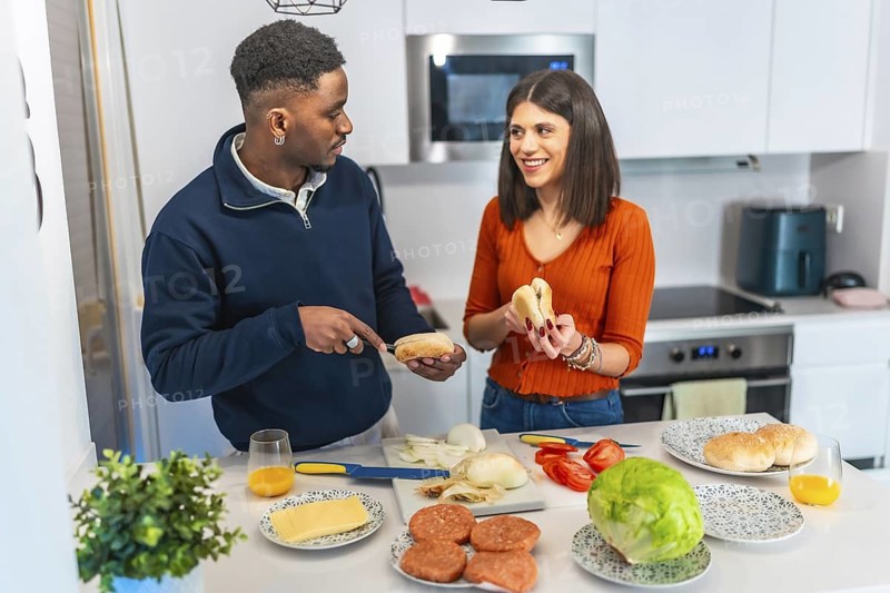 Young multiethnic couple preparing burgers in a modern kitchen, enjoying their time together