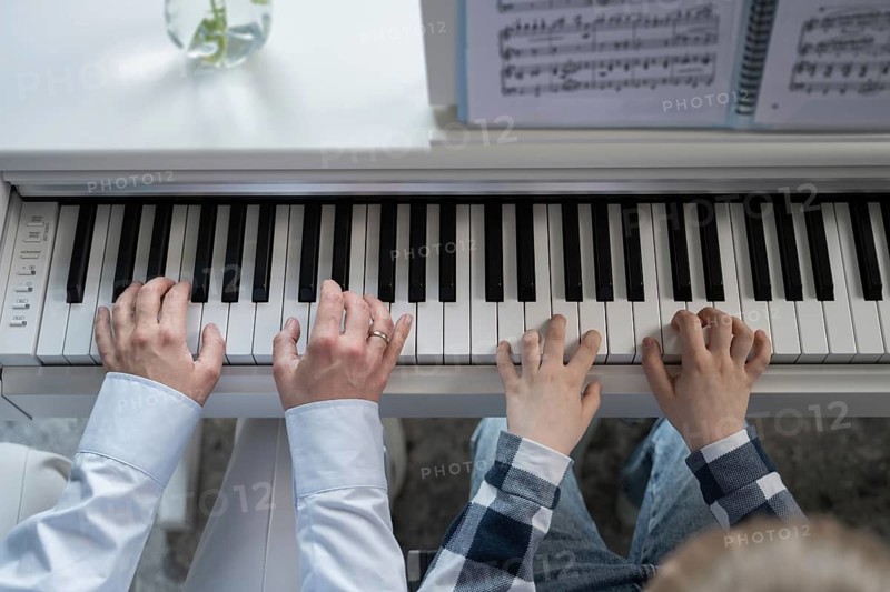 Close-up view of adult and child hands playing the piano together, emphasizing learning and teaching music. A beautiful scene of harmony and connection through music