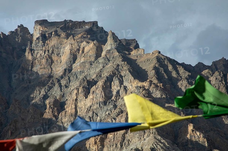 Mountain range in Spiti Valley, India, adorned with vibrant prayer flags fluttering in the wind under a gray sky, creating a serene and spiritual atmosphere