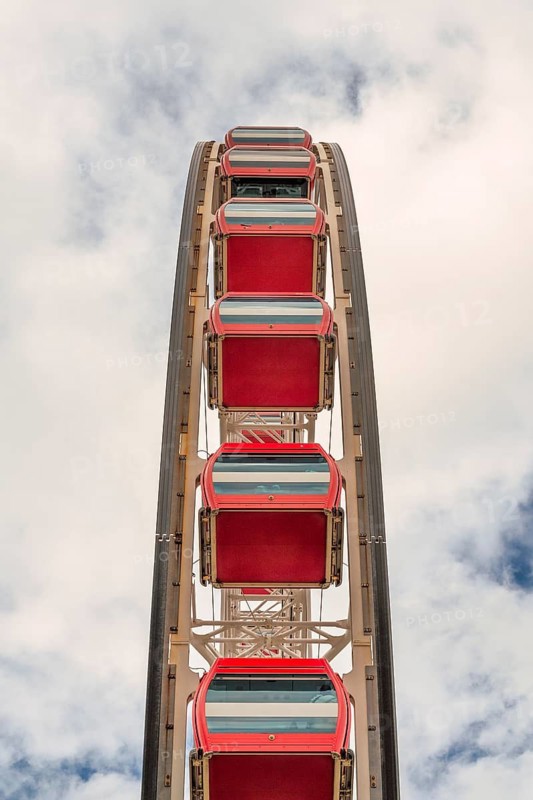 A vertical view of vibrant red Ferris wheel cabins against a soft cloudy backdrop in Hong Kong, illustrating a quiet, scenic ride high above the urban landscape