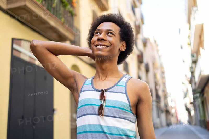 A joyful non-binary individual smiling brightly, enjoying a sunny day on a lively city street, exuding positivity and confidence. Dressed casually, they embrace the moment
