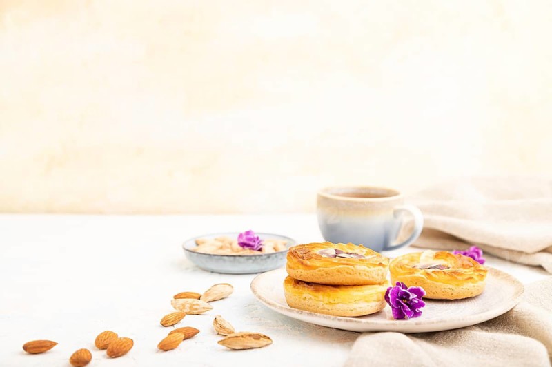 Small cheesecakes with jam and almonds with cup of coffee on a white concrete background and linen textile. Side view, copy space