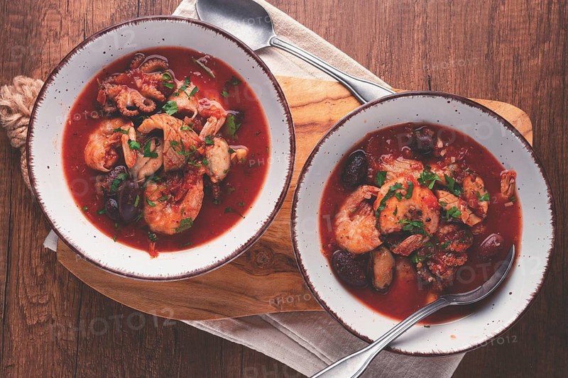 Two plates of seafood in tomato sauce, olives, top view