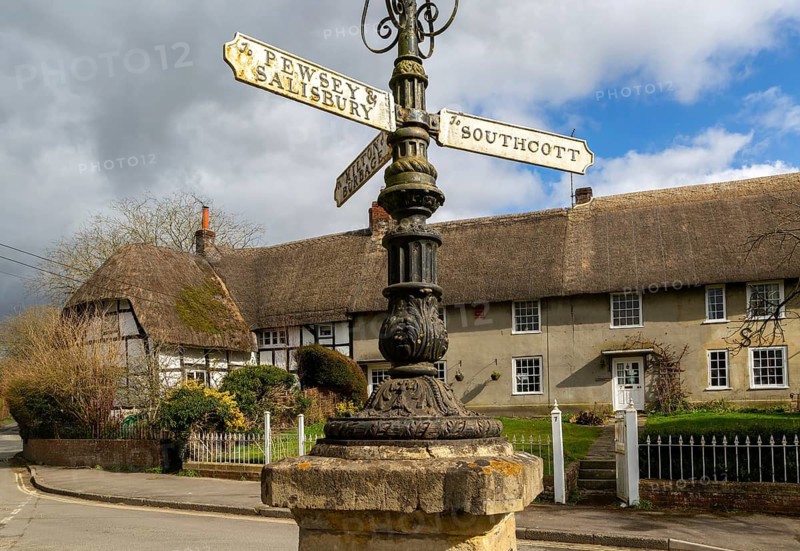 Historic signpost with direction painters, thatched cottages in village of Pewsey, Wiltshire, England, UK