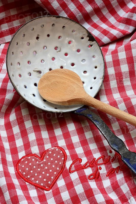 Dish drainer and cooking spoon on kitchen towel with lettering 'Cucina di mamma'